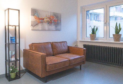 Leather sofa with coffee color, painting and flowers nearby the window in the Natalie Herzel Dental Clinic